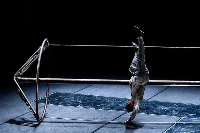 Una persona está haciendo una parada de manos en una barra en una habitación oscura.