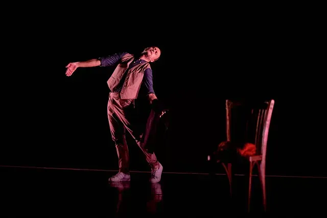 Un hombre está bailando frente a una silla en una habitación oscura.