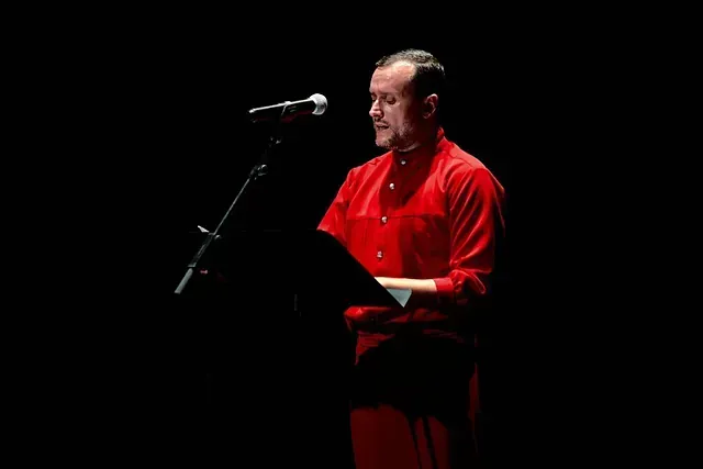 Un hombre con una camisa roja está de pie en un podio hablando a través de un micrófono.