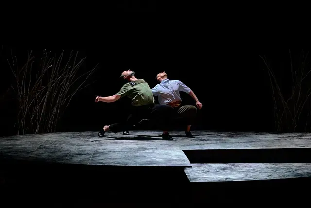 Dos hombres bailan en un escenario en la oscuridad.