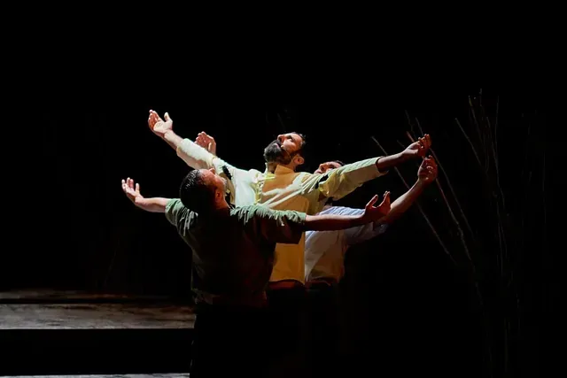 Un grupo de hombres baila en un escenario con los brazos extendidos.