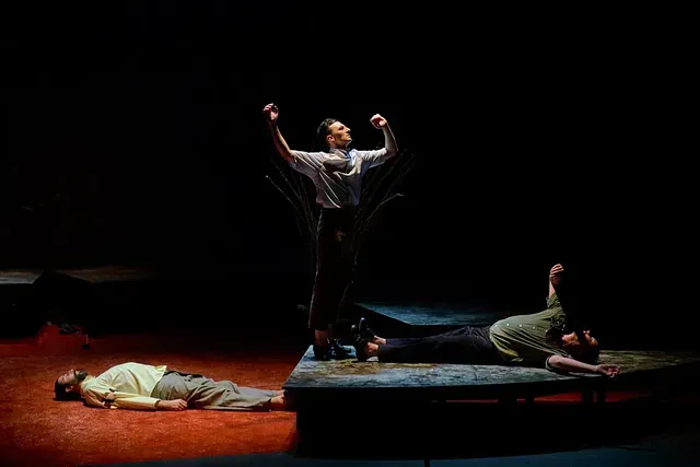 Un hombre está de pie en un escenario al lado de un hombre tendido en el suelo.