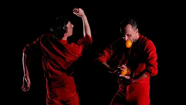 Dos personas vestidas con monos rojos sostienen una naranja en sus manos.