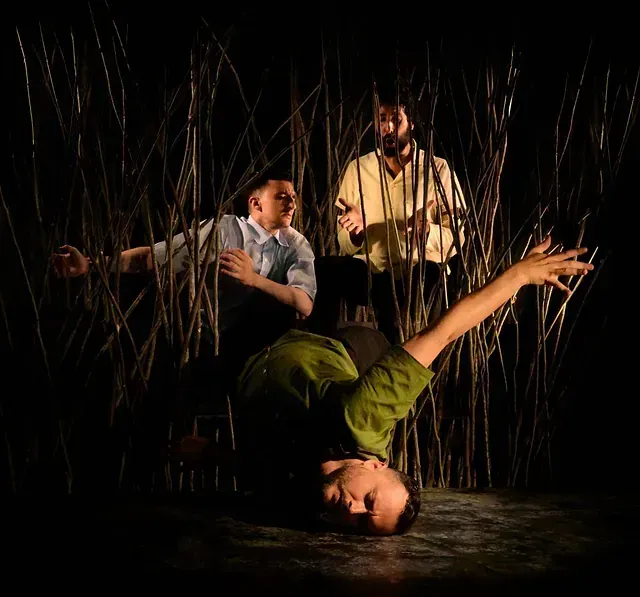 Un hombre con una camisa verde está haciendo una parada de manos en una habitación oscura.
