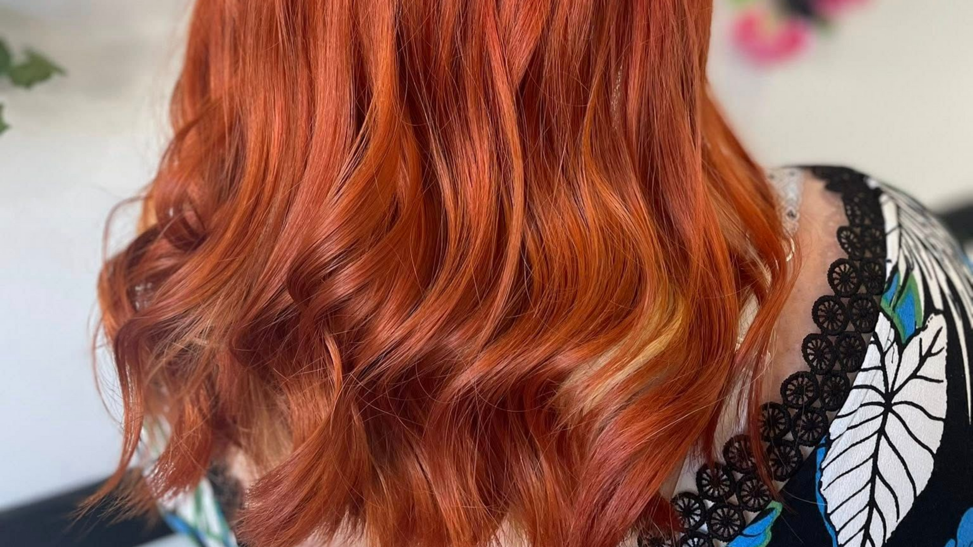 Cheveux roux ondulés mi-longs. Personne partiellement visible portant un haut à motifs.