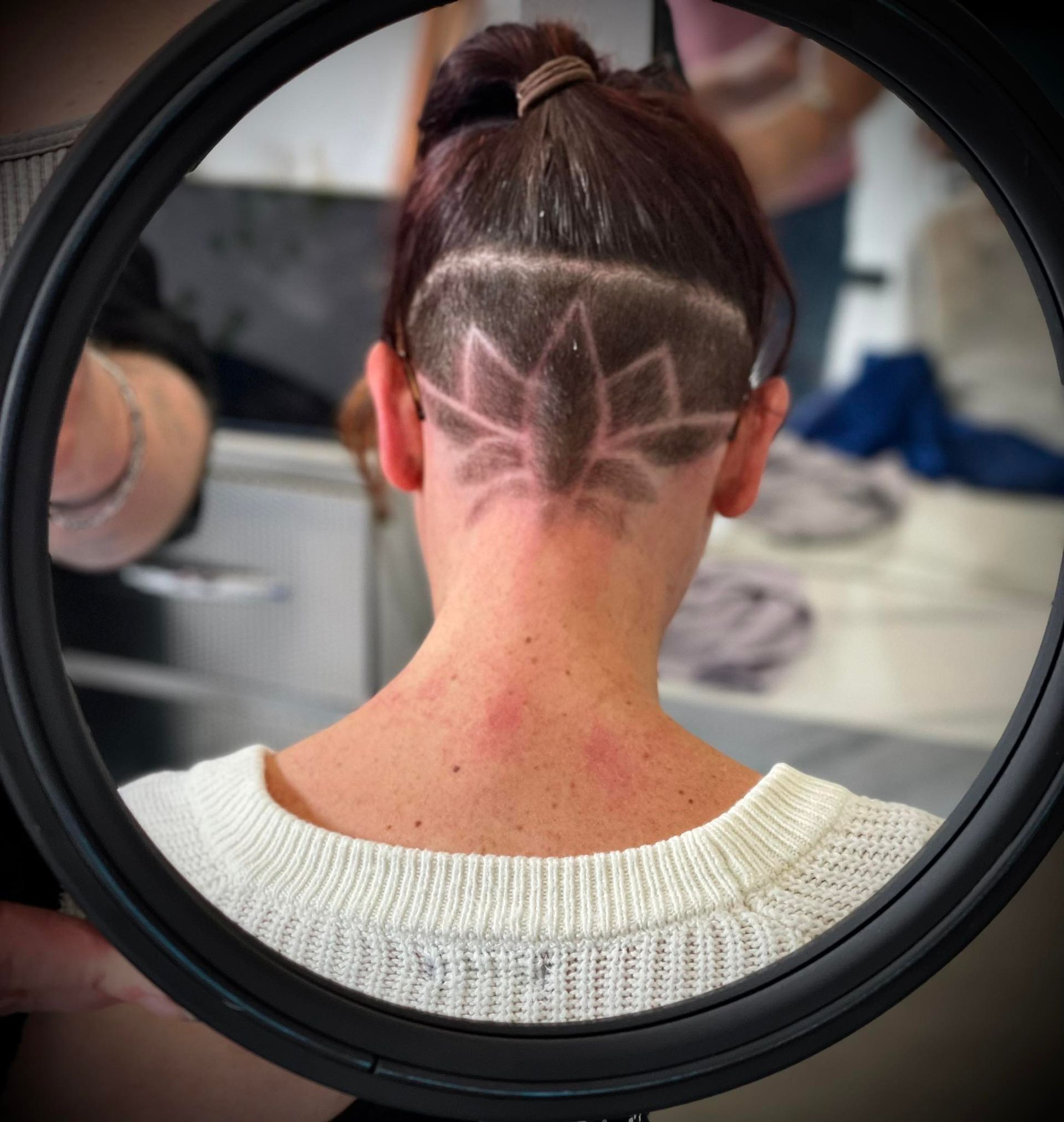 Personne avec un motif de soleil rasé à l'arrière de ses cheveux foncés.