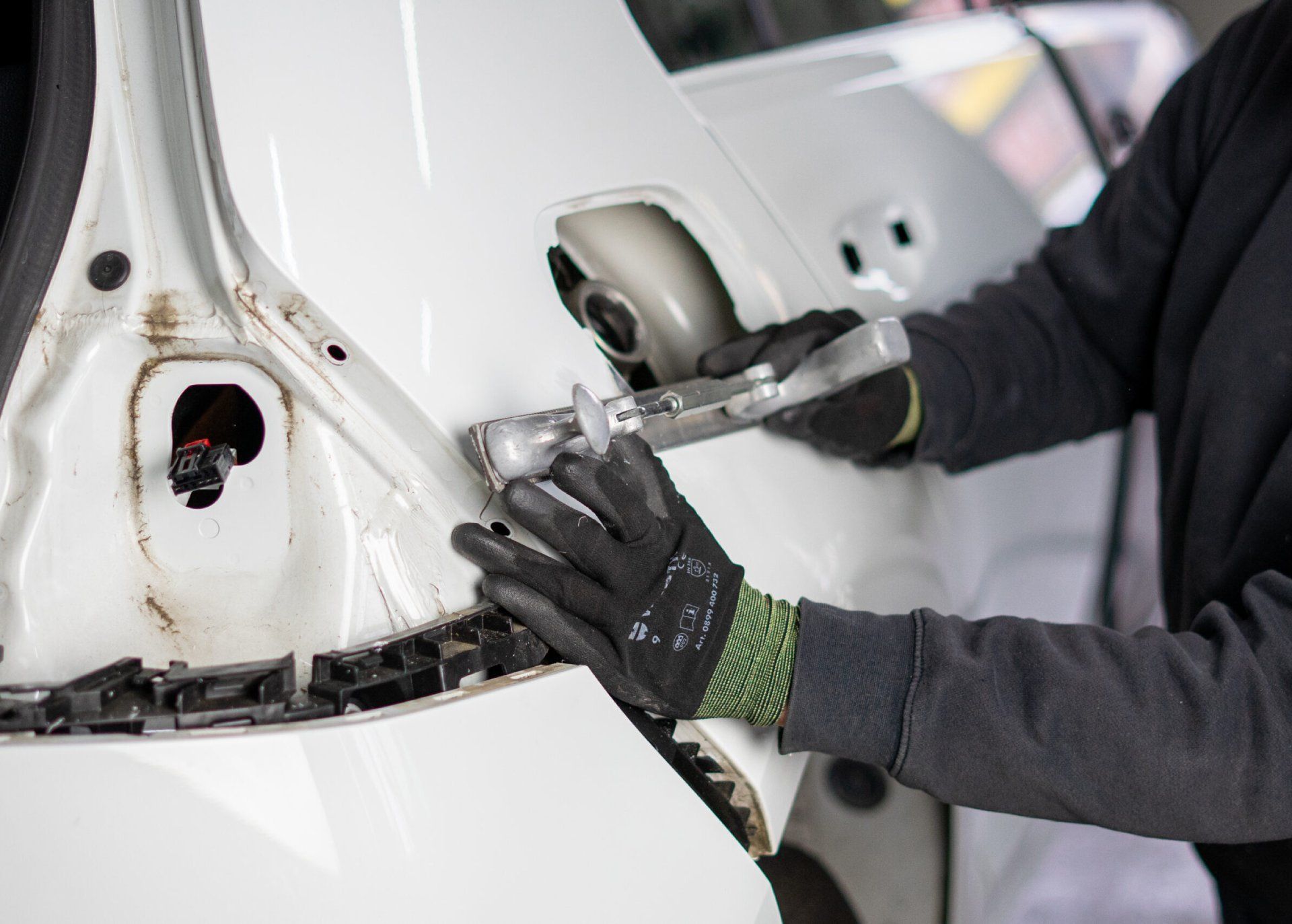 Ein Techniker repariert mit einem Metallwerkzeug die Heckklappe eines weissen Autos.