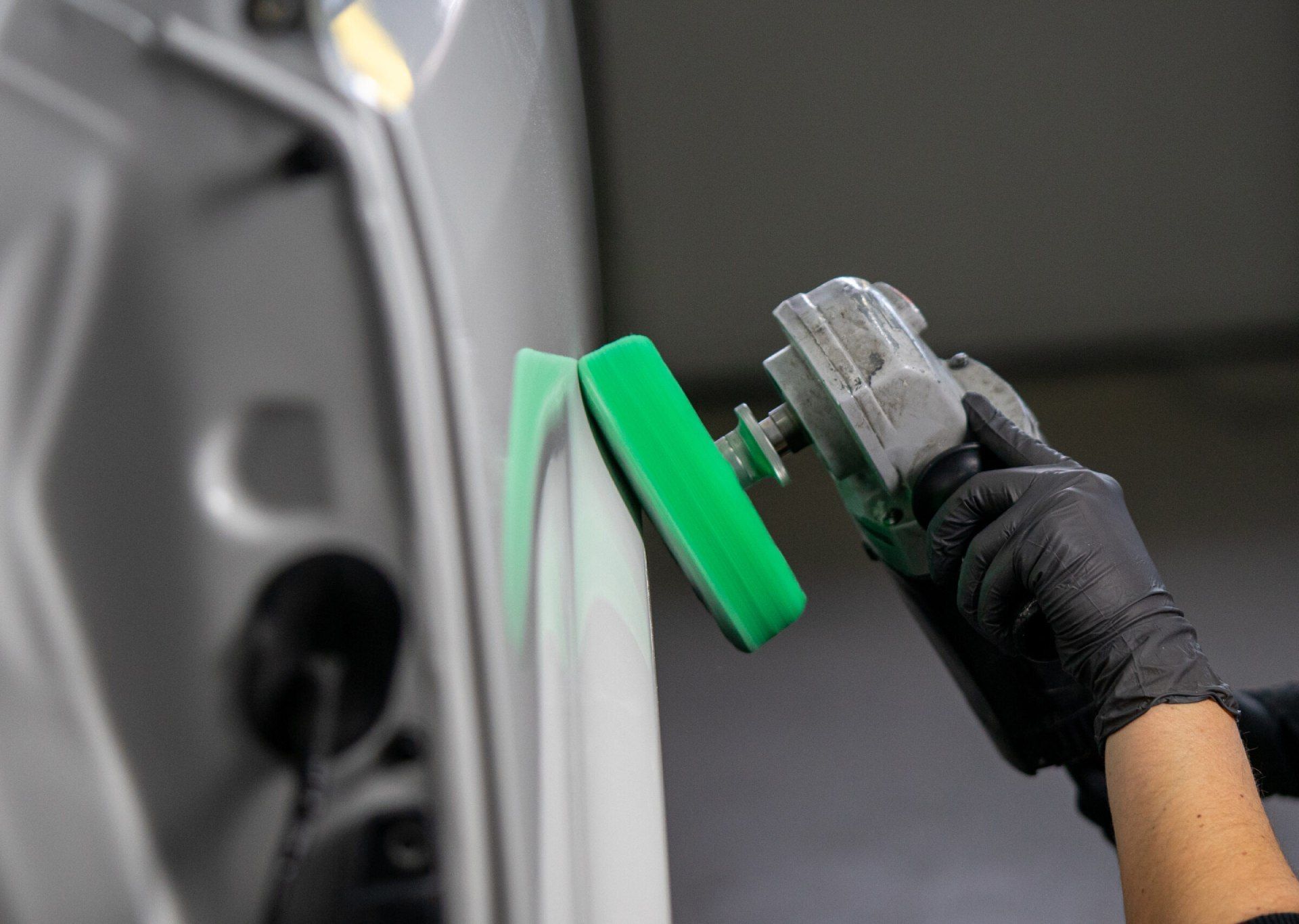 Eine behandschuhte Hand poliert eine Autotür mit einem grünen Polierpad.