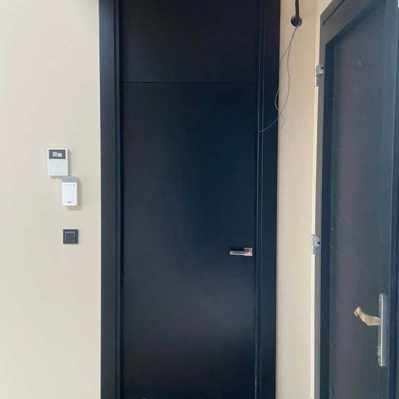 Una puerta negra está en un pasillo al lado de una pared blanca.