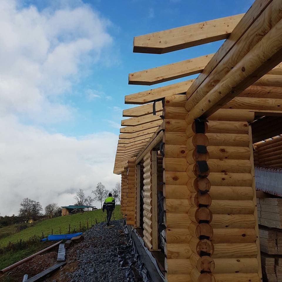 Un hombre está parado frente a una cabaña de troncos en construcción.