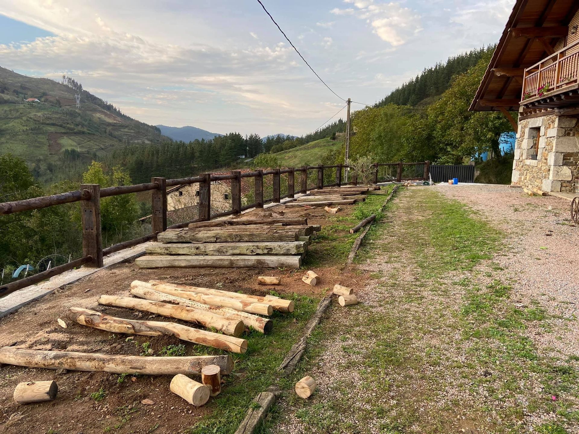 Una pila de troncos está en el césped al lado de una valla de madera.