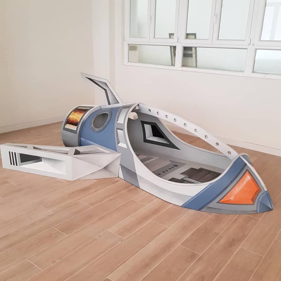 Una cama que parece una nave espacial está colocada sobre un piso de madera en una habitación.