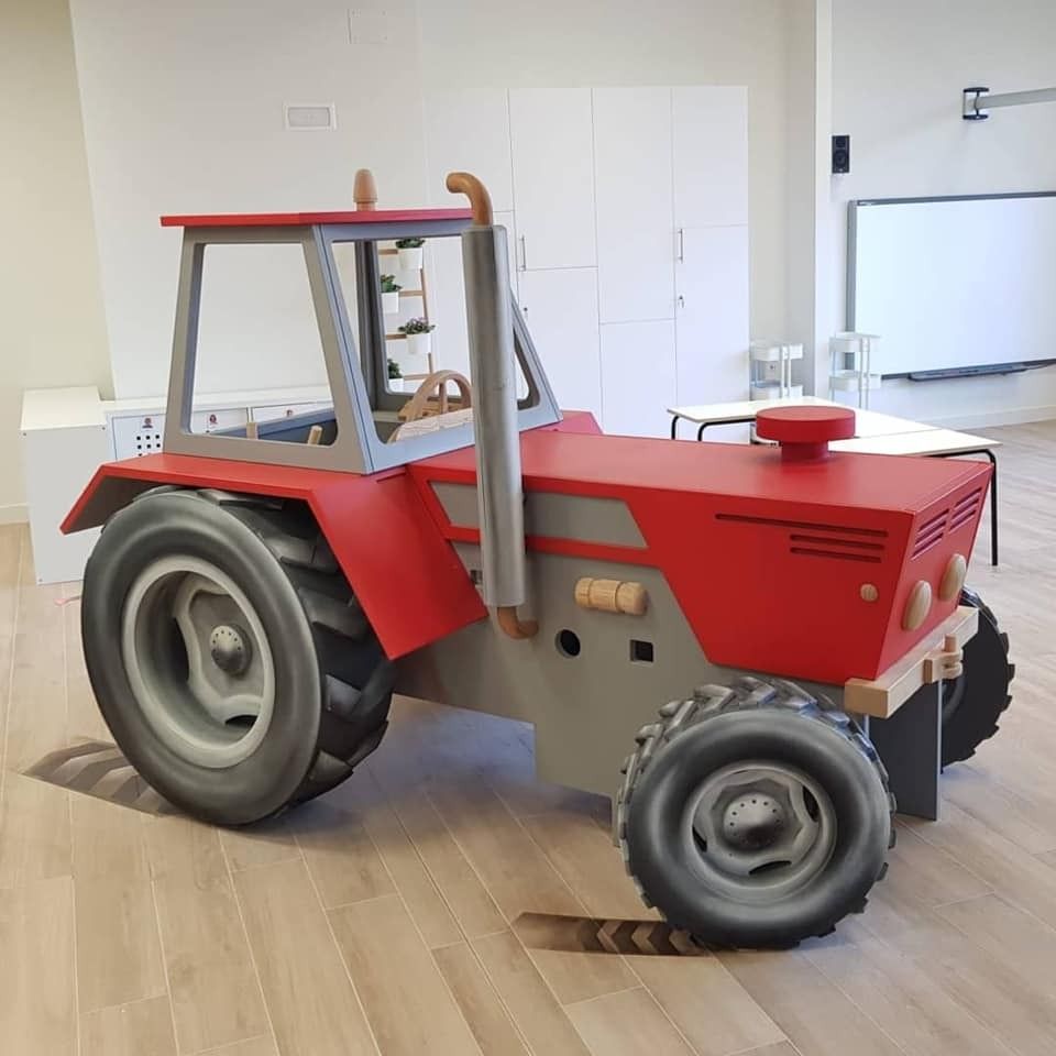 Un tractor rojo está sentado sobre un piso de madera en una habitación.