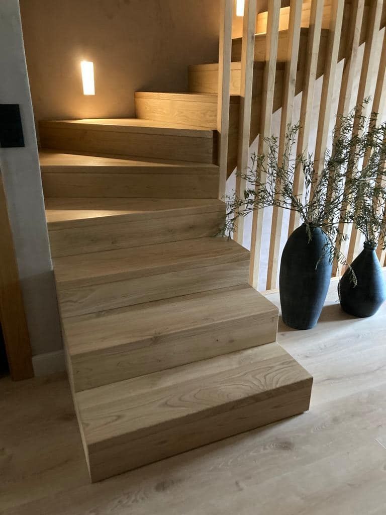 Una escalera de madera con barandilla de madera y jarrones en los escalones.