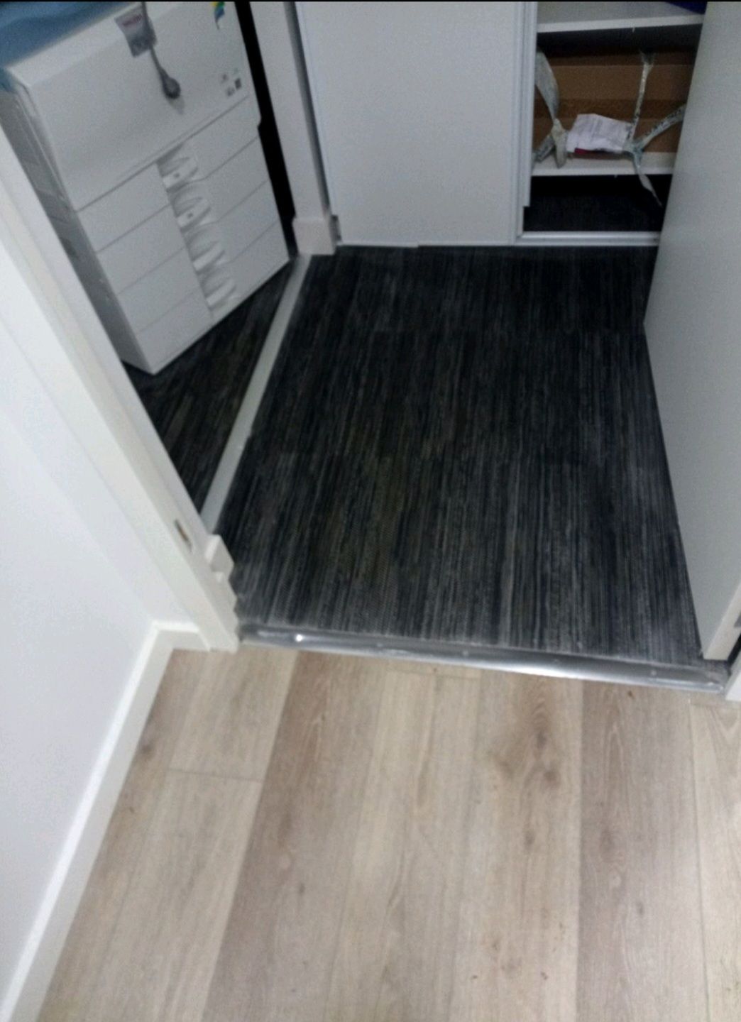 Couloir menant à une petite salle de bains, avec une imprimante et une chaise au premier plan, après nettoyage.