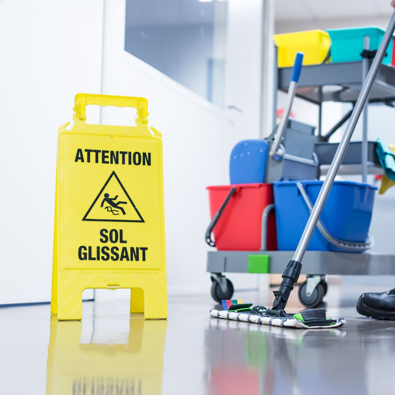 Panneau jaune « sol mouillé » à côté du chariot de nettoyage et de la serpillière sur le sol brillant.