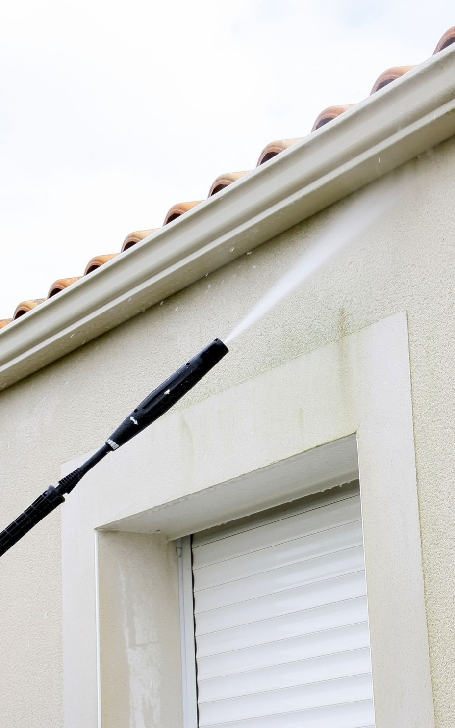 Nettoyeur à haute pression pulvérisant le mur extérieur d'un bâtiment près d'une gouttière ; éliminant la végétation verte.