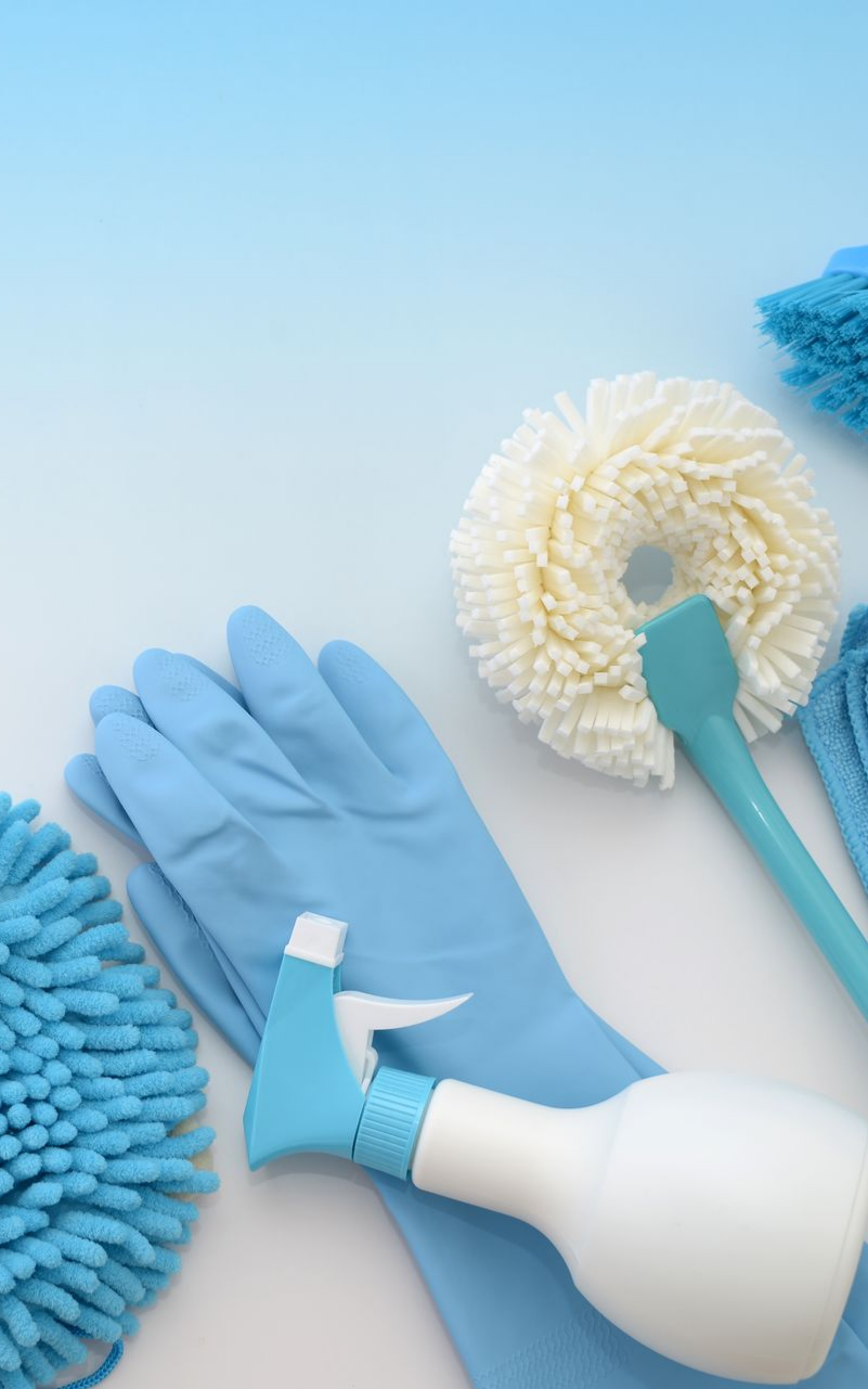 Produits de nettoyage bleus, notamment gants, flacon pulvérisateur et brosses à récurer, sur un fond dégradé blanc et bleu.