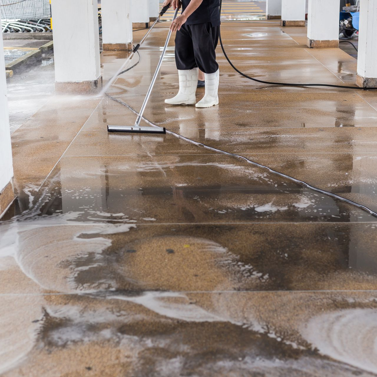 Une personne nettoie à haute pression un sol en béton mouillé dans un bâtiment.