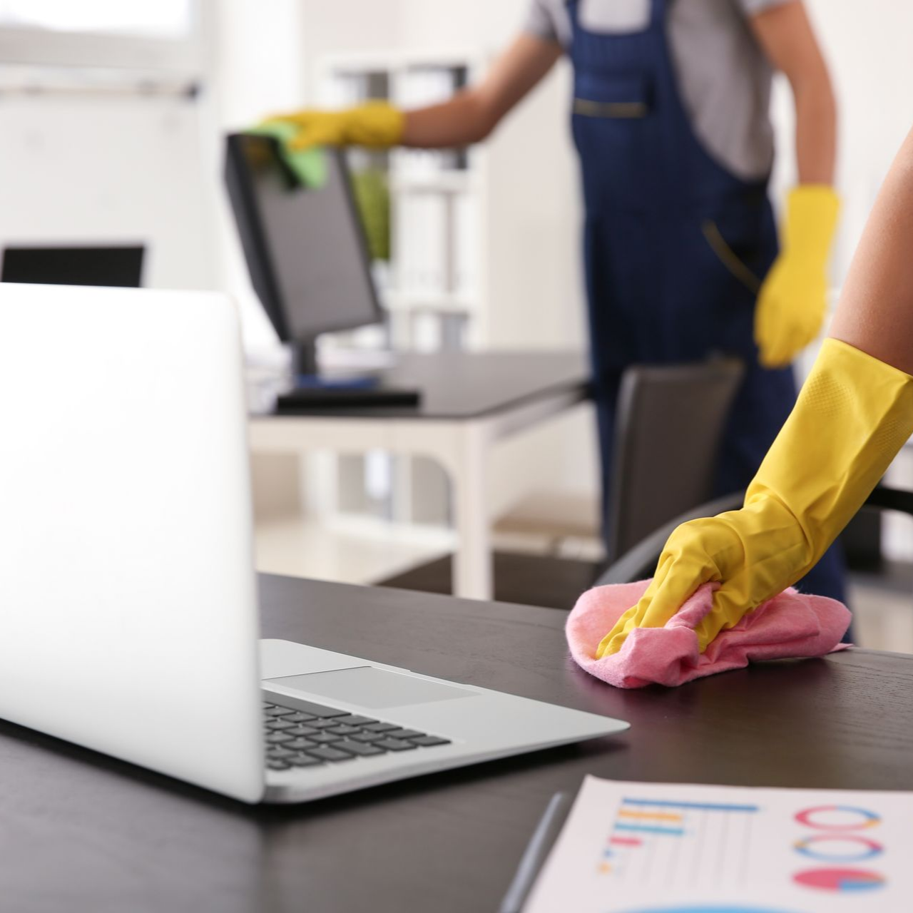 Deux personnes portant des gants jaunes nettoient des bureaux avec des chiffons.