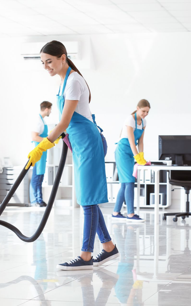 Trois agents d'entretien portant des tabliers passent l'aspirateur et nettoient les surfaces des bureaux.