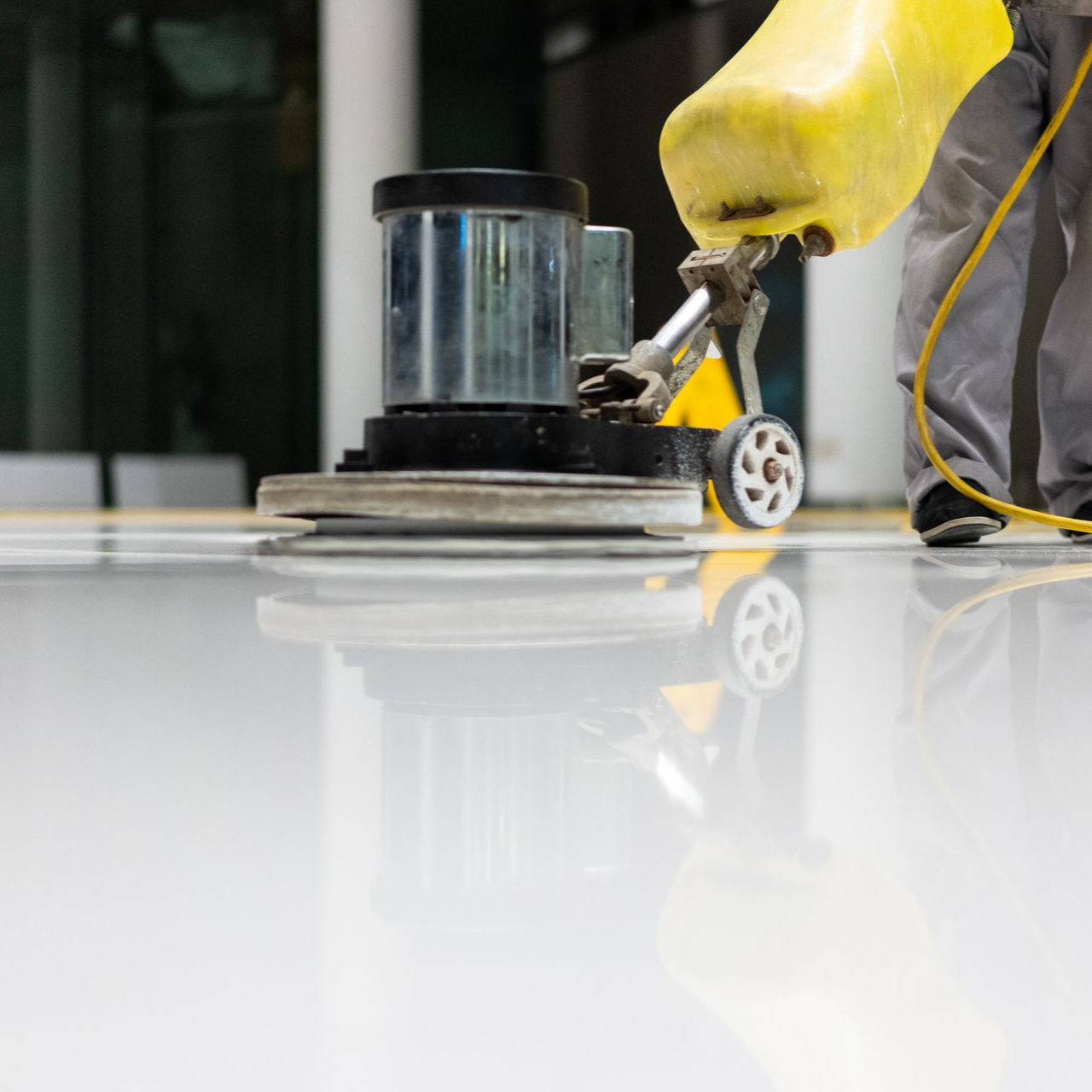 Une personne utilise une polisseuse de sol jaune pour faire briller un sol blanc très réfléchissant.