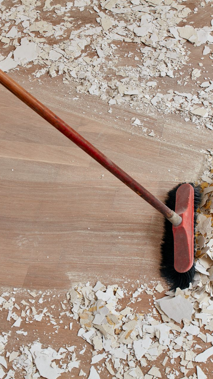 Balai balayant des débris sur une surface en bois, avec des flocons blancs épars autour des poils et du manche.