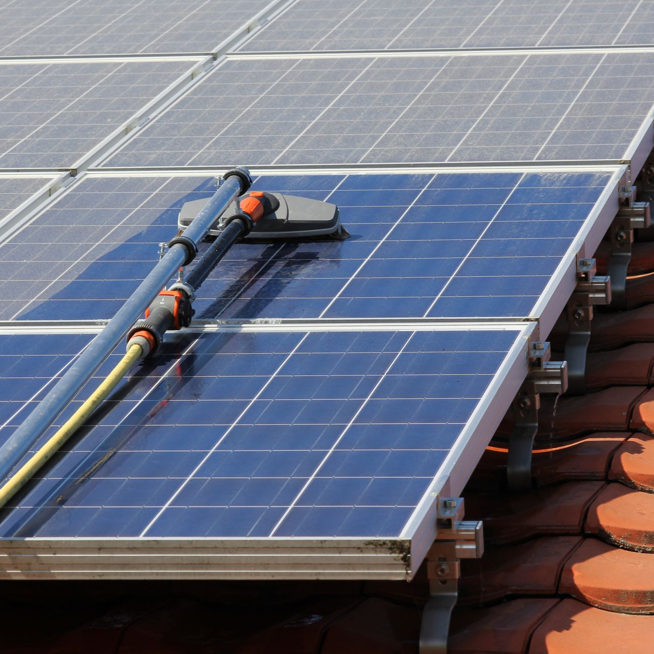 Nettoyage de panneaux solaires sur un toit à l'aide d'une brosse à long manche et d'eau.