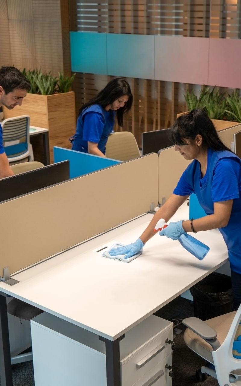 Personnel de nettoyage nettoyant les bureaux. Chemises bleues, gants, cloisons aux tons neutres et un cadre de bureau moderne.