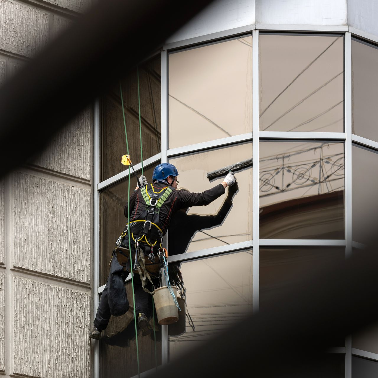 Laveur de vitres sur un immeuble, suspendu par des cordes, utilisant une raclette sur la vitre.