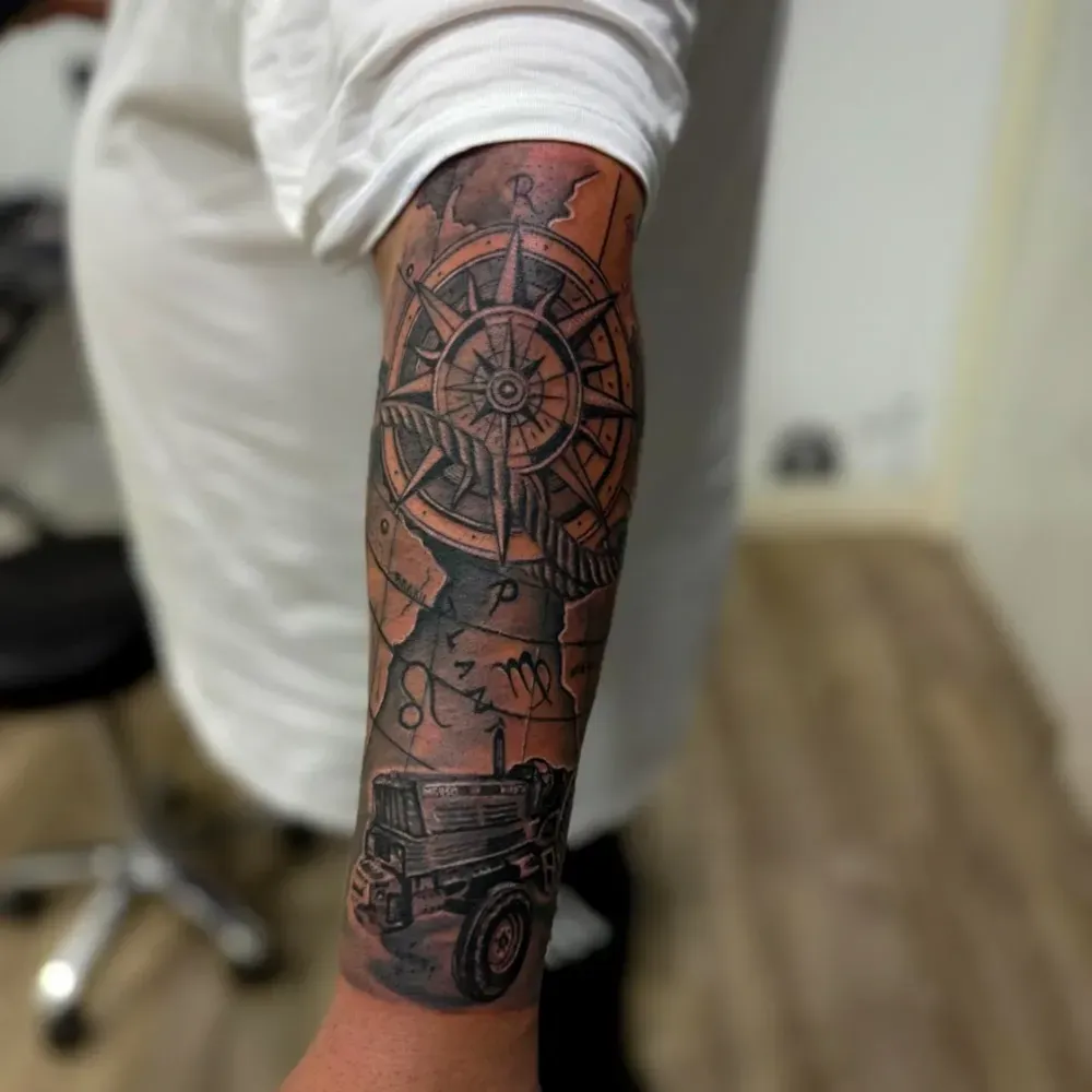 Tatuaje de una rosa de los vientos, un mapa y un todoterreno en el brazo. Tinta gris y negra.