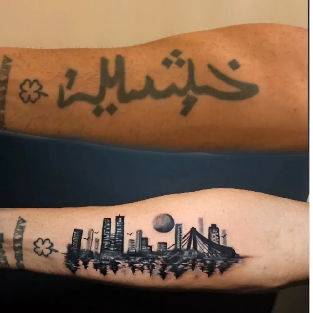Tatuaje encubierto: antes, escritura árabe descolorida; después, paisaje urbano negro con reflejo de la luna sobre el agua.