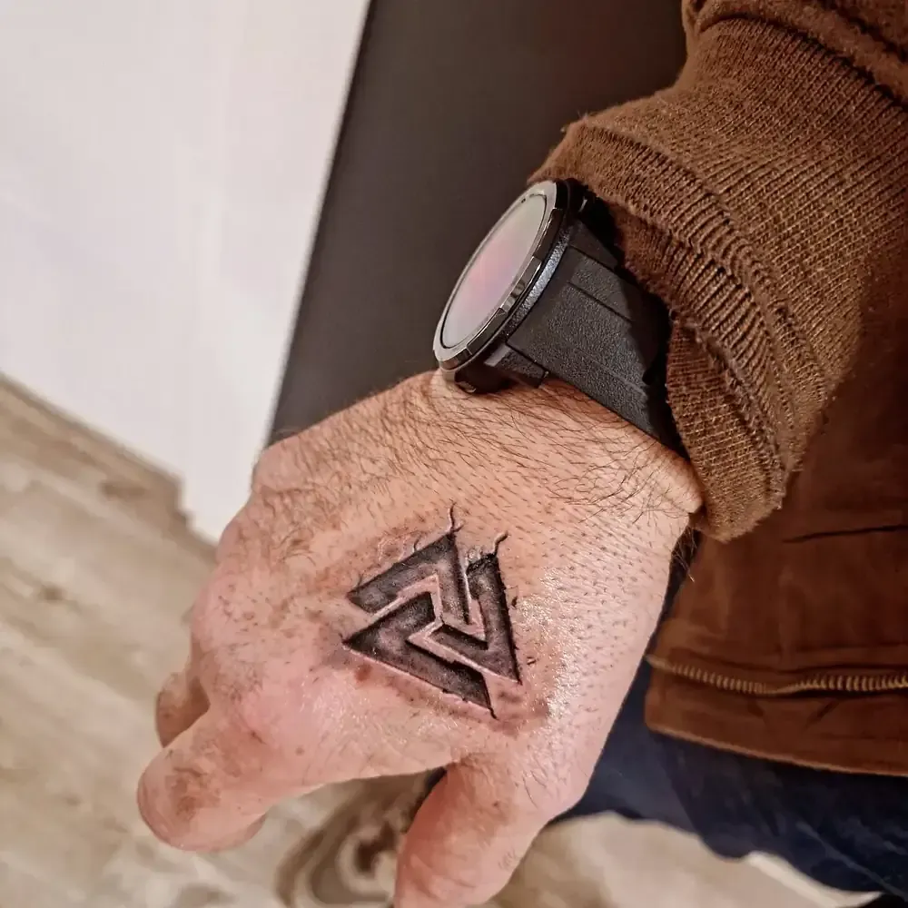 Mano con un tatuaje de símbolo de triángulo y un reloj.