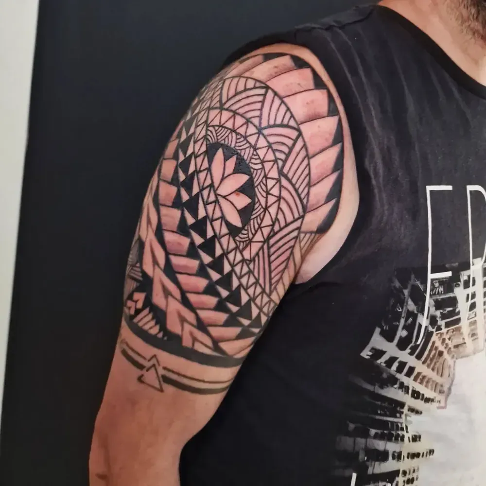 Brazo con tatuaje geométrico negro, vistiendo una camiseta negra sin mangas.