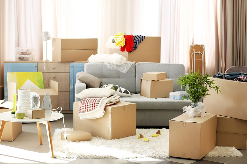 Ein Zimmer voller Umzugskartons, die um eine Couch und einen Tisch mit Haushaltsgegenständen herum angeordnet sind.