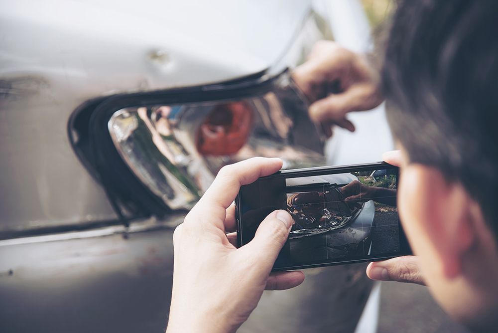 Eine Person fotografiert mit einem Smartphone ein beschädigtes silbernes Autorücklicht.