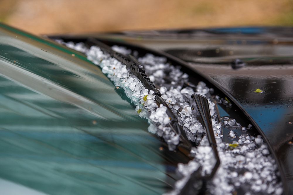 Ein Haufen weißer Hagelkörner sammelt sich an der Windschutzscheibe und den Scheibenwischern eines schwarzen Autos.