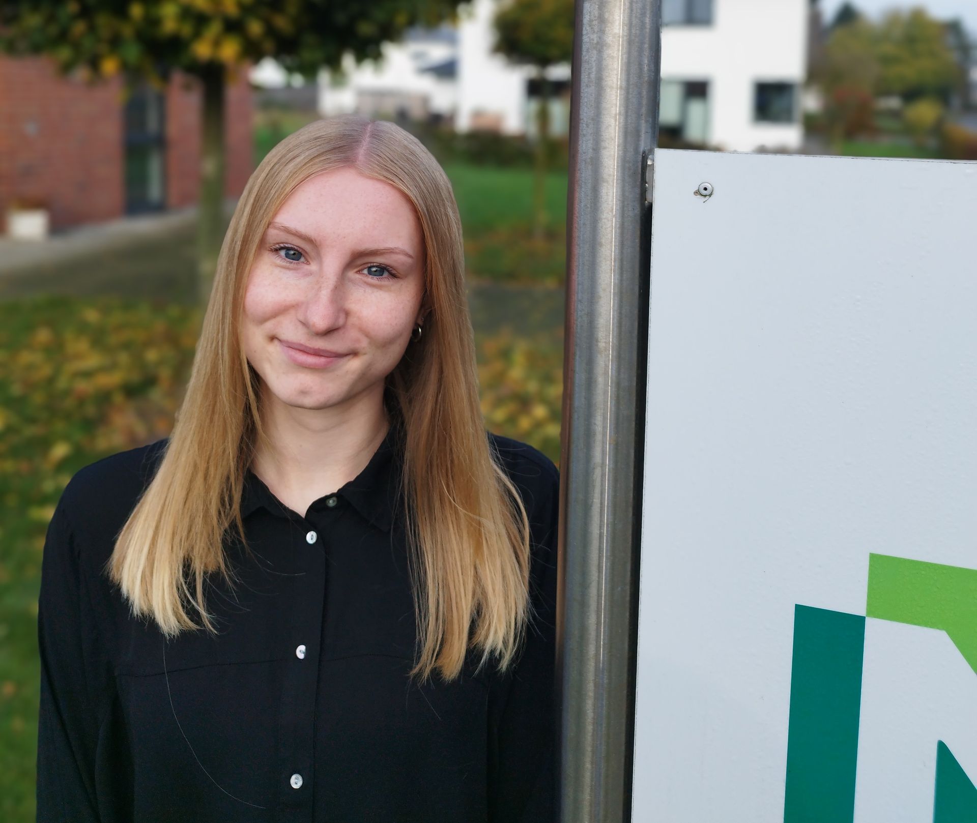 Eine Frau in einem schwarzen Hemd steht neben einem Schild.