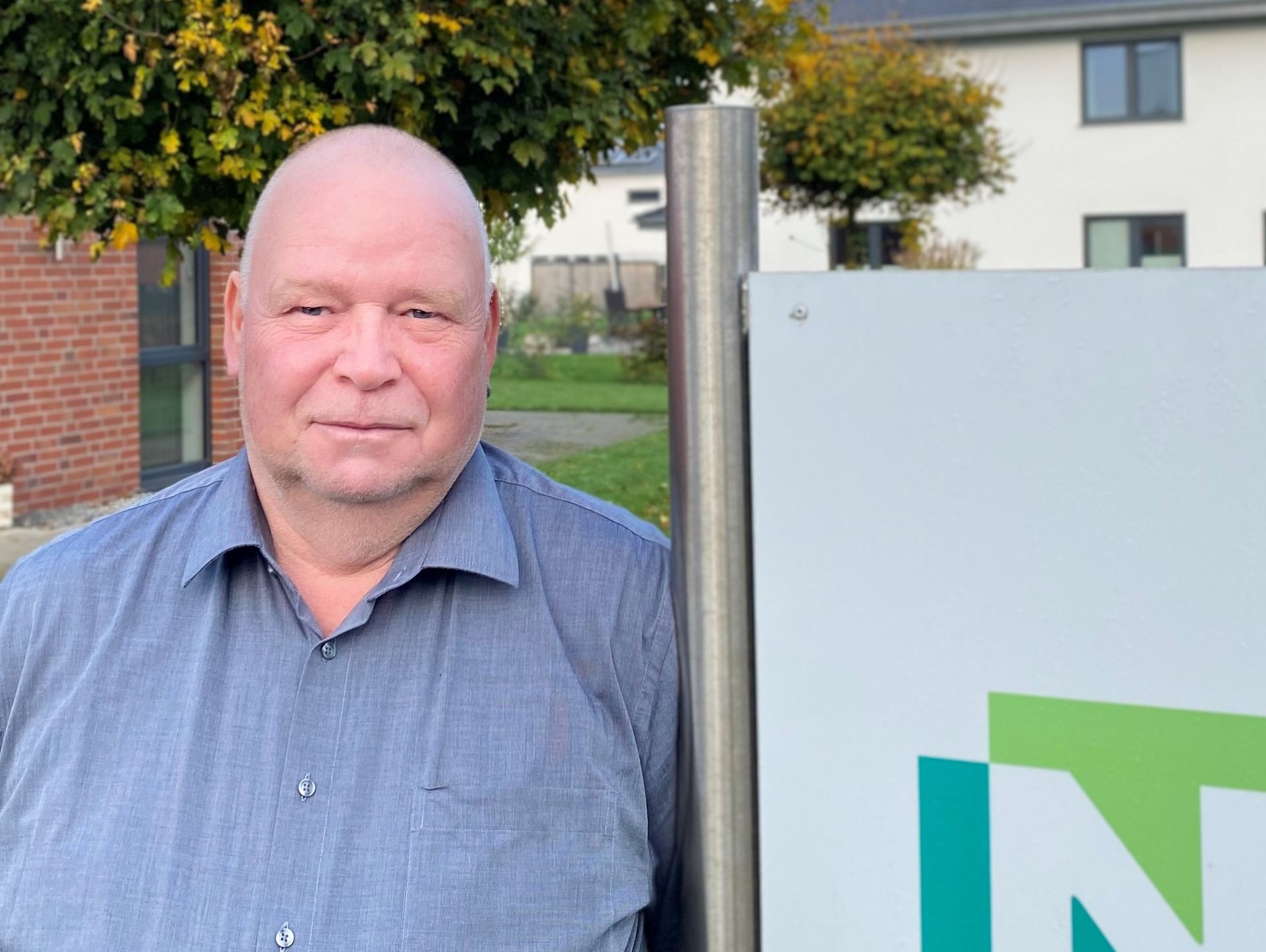 Ein Mann in einem blauen Hemd steht vor einem Schild mit dem Buchstaben „N“ darauf.