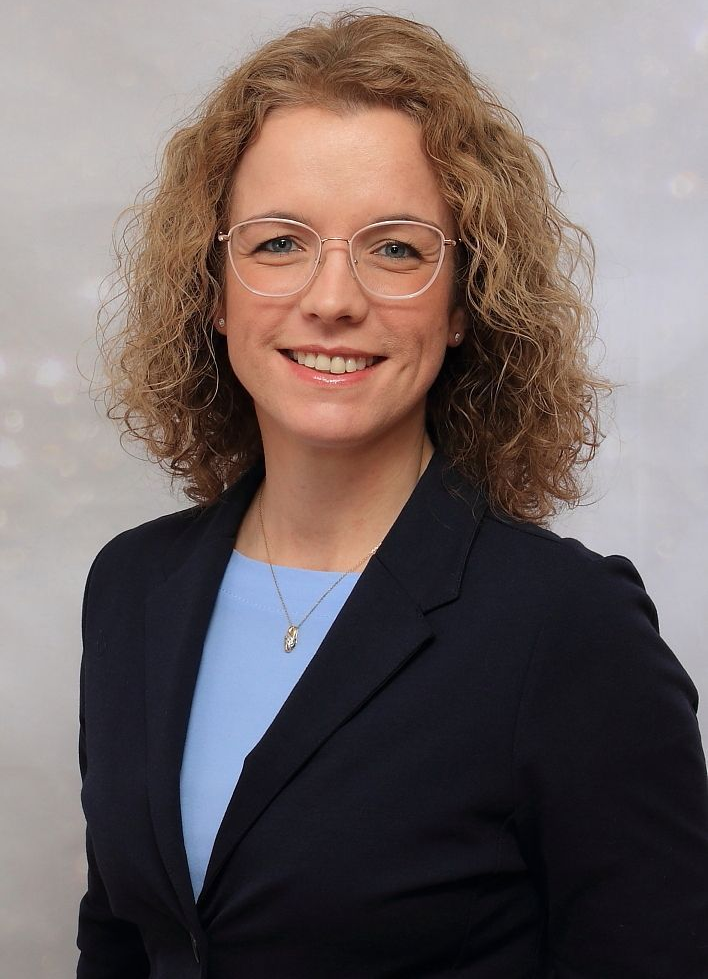 Ein Mann in einem blauen Hemd steht lächelnd neben einem Schild