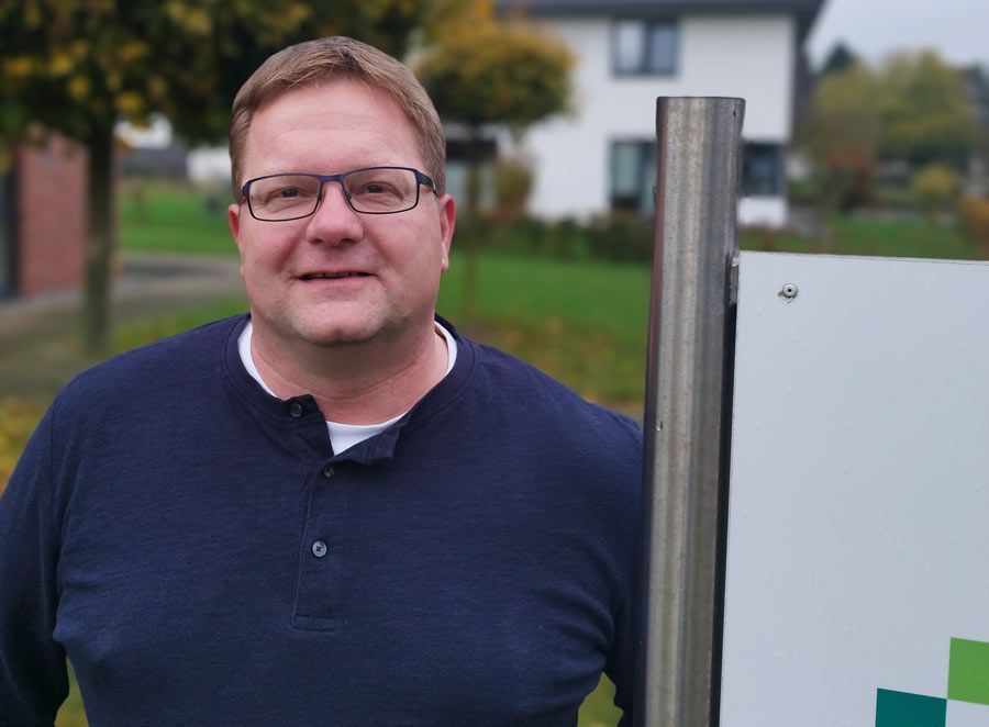 Ein Mann in einem blauen Hemd steht lächelnd neben einem Schild