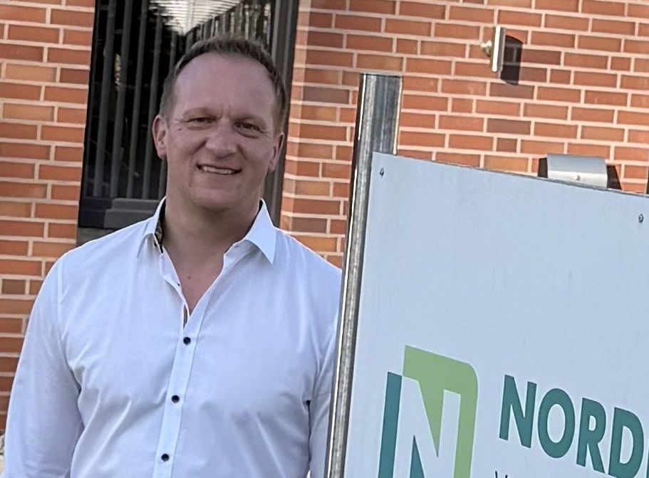 Ein Mann in einem blauen Hemd steht neben einem Schild.