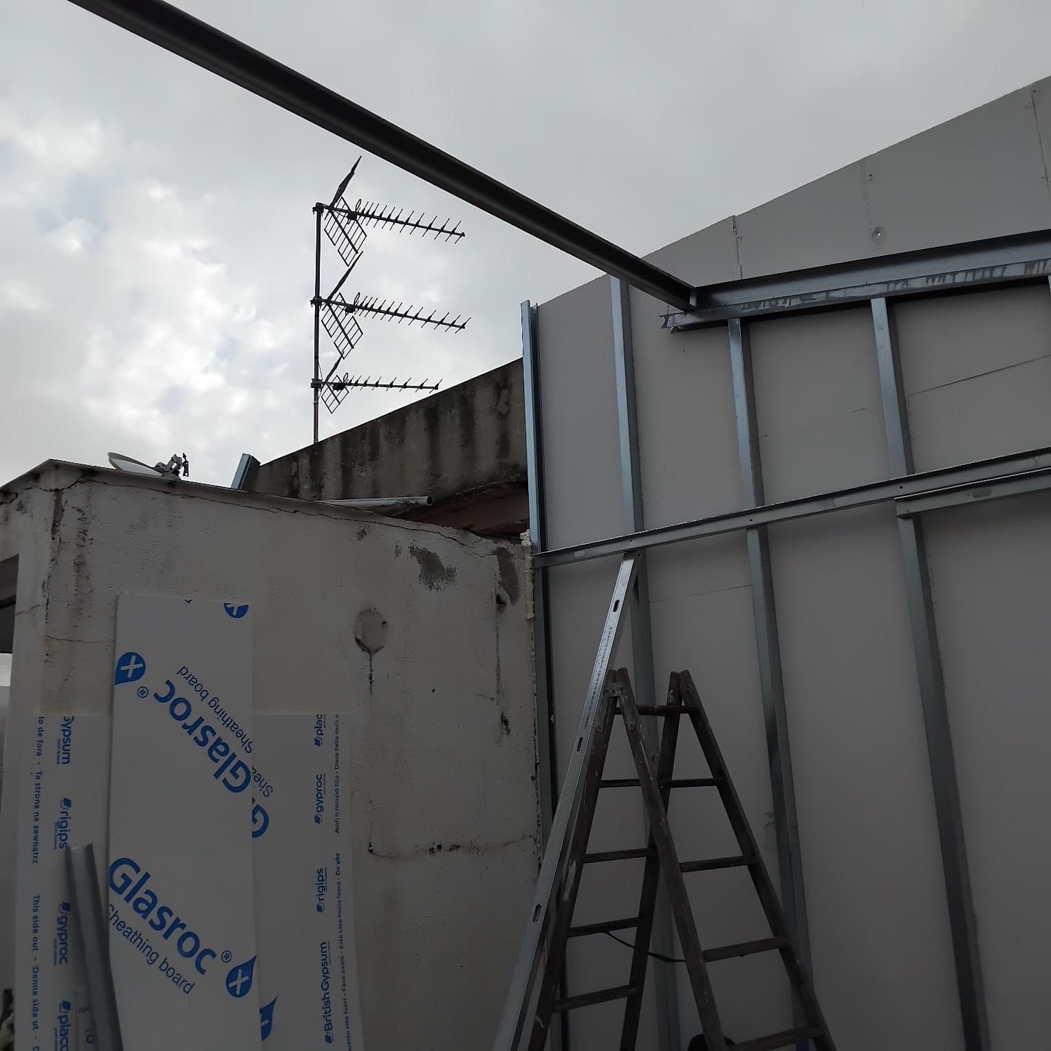 Sitio de construcción con estructura de metal, escalera y paneles de aislamiento contra un cielo nublado.