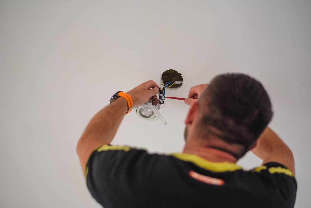 Persona con camisa negra, instalando una lámpara de techo con un destornillador.