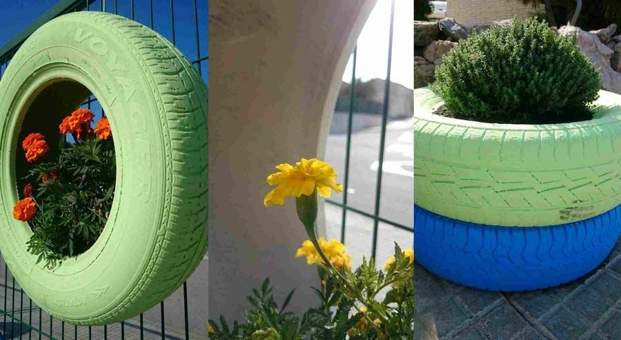 Tres jardineras de neumáticos de colores con flores: neumático verde en la cerca, flor amarilla en el frente, jardinera de neumáticos apilados azul/verde.