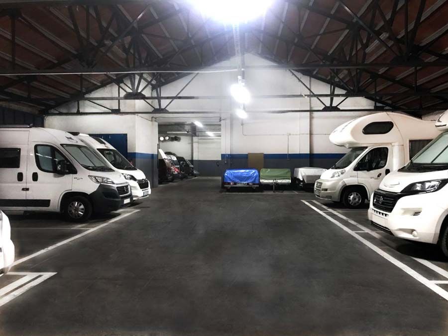 Furgonetas camper blancas estacionadas dentro de un garaje con piso gris oscuro y luces en el techo.