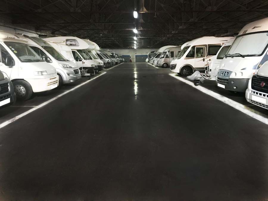 Filas de vehículos recreativos blancos estacionados en un depósito interior largo y poco iluminado.