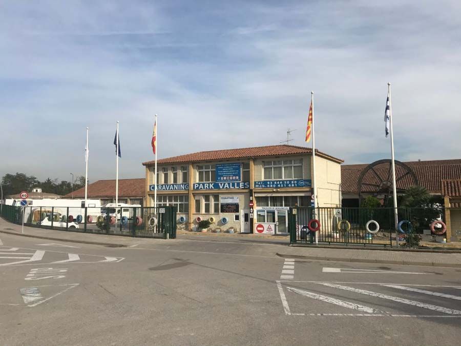 Edificio de dos pisos con banderas, entrada y camino; los carteles dicen 