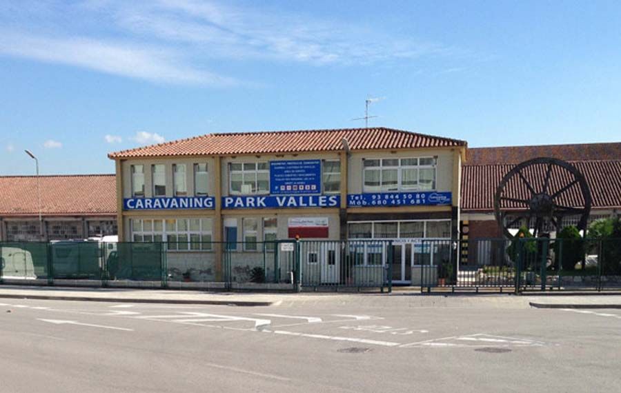 Edificio del Caravaning Park Valles con cartel, entrada y gran equipo en el frente, contra un cielo azul.