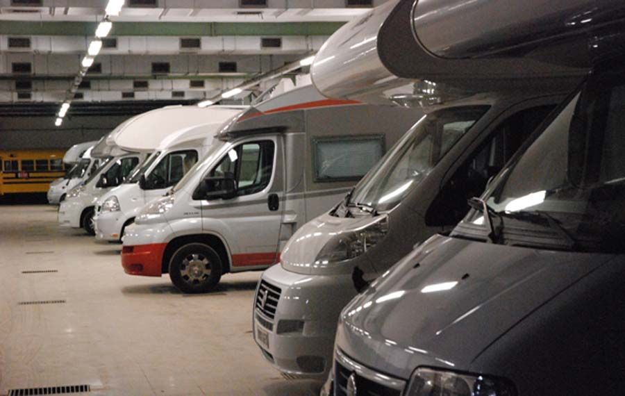 Autocaravanas estacionadas en una instalación de almacenamiento interior bien iluminada, una al lado de la otra, varios modelos blancos y grises.
